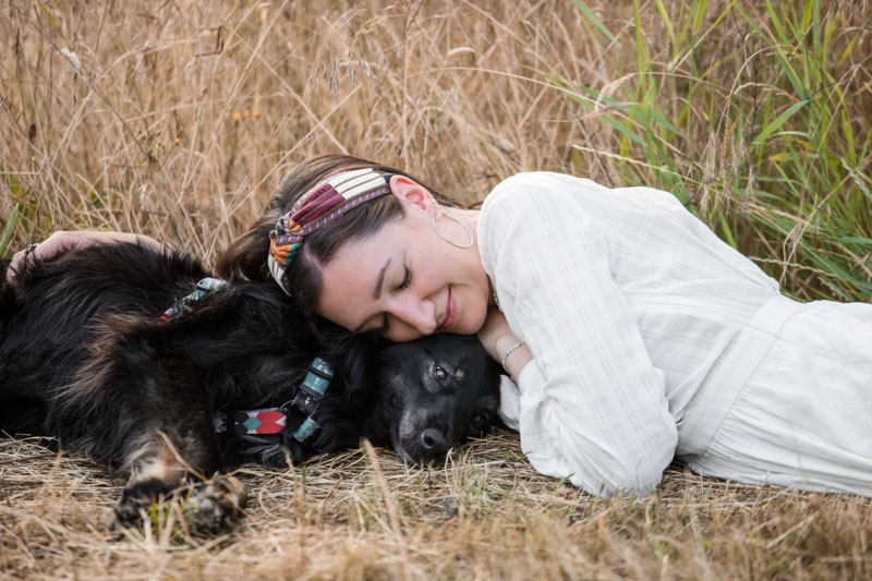 Besitzerin kuschelt ihren Hund im Liegen im Gras