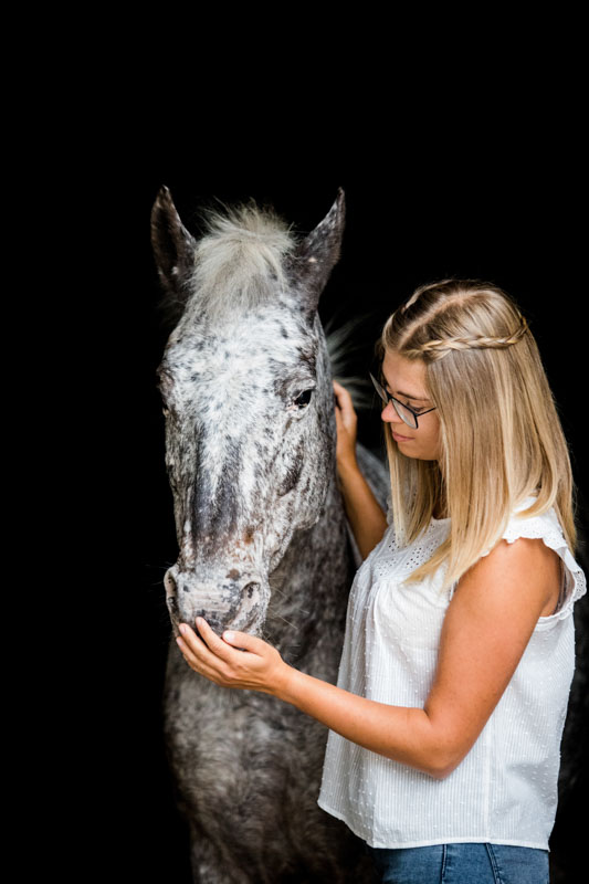 Besitzerin mit ihrem Pferd vor schwarzem Hintergrund im Portrait